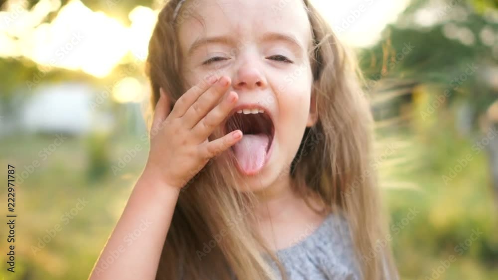 Todler girl opens her mouth wide, baby teeth are visible, she laughs cheerfully. A close portrait against the backdrop of the setting sun, summer day. Children's health Todler girl opens her mouth wide, baby teeth are visible, she laughs cheerfully. A close portrait against the backdrop of the setting sun, summer day. Children's health
