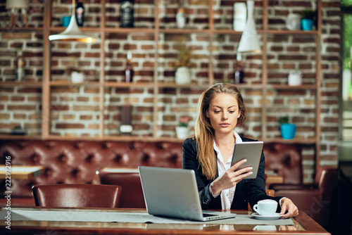 Businesswoman using tablet while sitting in cafeteria. On table laptop and coffee.