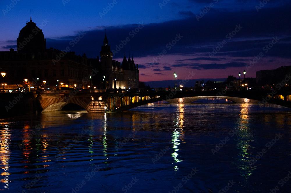 Blue hour in Paris. View of Pont au Change bridge and Conciergerie building. Colorful reflection of evening city lights in Seine river water.