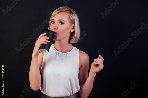 Businesswoman blonde in a white blouse with coffee or tea in black plastic cup studio shot