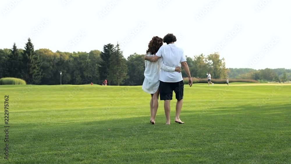Couple in love hugging, walking outdoors in the park on the green grass. Steadycam shot. Couple in love hugging, walking outdoors in the park on the green grass. Steadycam shot.