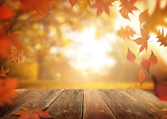 A rustic old wooden table outdoors with autumn leaves falling in the background.