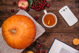 Top view of a  pumpkin, apples and a book, phone on wooden table.