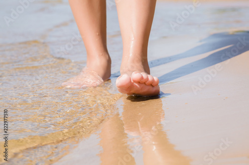 Young woman's barefoot walking on the beach at the sea in sunny summer day.