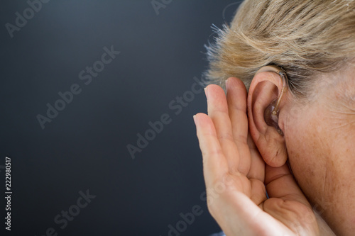 Elderly woman with hearing aid on grey background. Deafness concept. photo