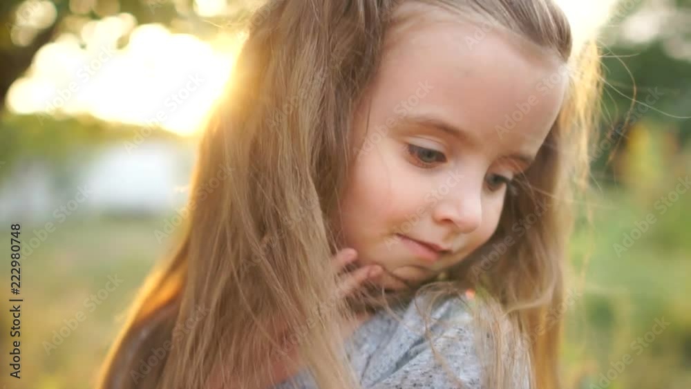A beautiful close portrait of a beautiful little girl with long hair and gray eyes. Baby corrects hair and lowers down long eyelashes A beautiful close portrait of a beautiful little girl with long hair and gray eyes. Baby corrects hair and lowers down long eyelashes