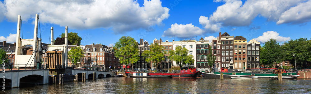 Beautiful panoramic panorama of the skinny bridge (magere brug) while open over the river Amstel in Amsterdam, the Netherlands, on a sunny summer day with some clouds
