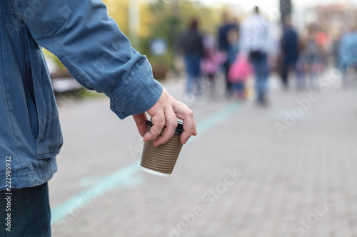 Close-up image of young hipster man walking at night city streets and drinking coffee to go outside, man wearing casual hoodie and enjoying his cappuccino