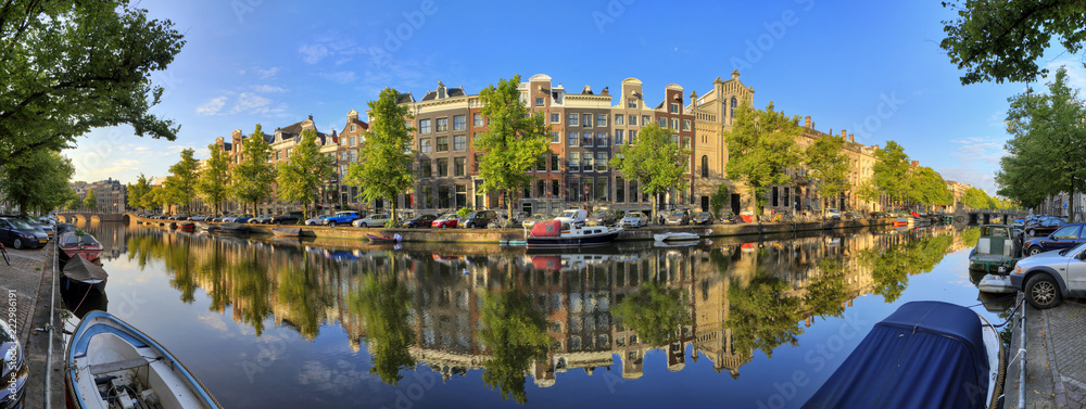Fototapeta premium Piękna panoramiczna panorama 180 stopni kanału Keizersgracht, wpisanego na listę światowego dziedzictwa UNESCO, w Amsterdamie w Holandii, w słoneczny letni dzień z błękitnym niebem i lustrzanym odbiciem