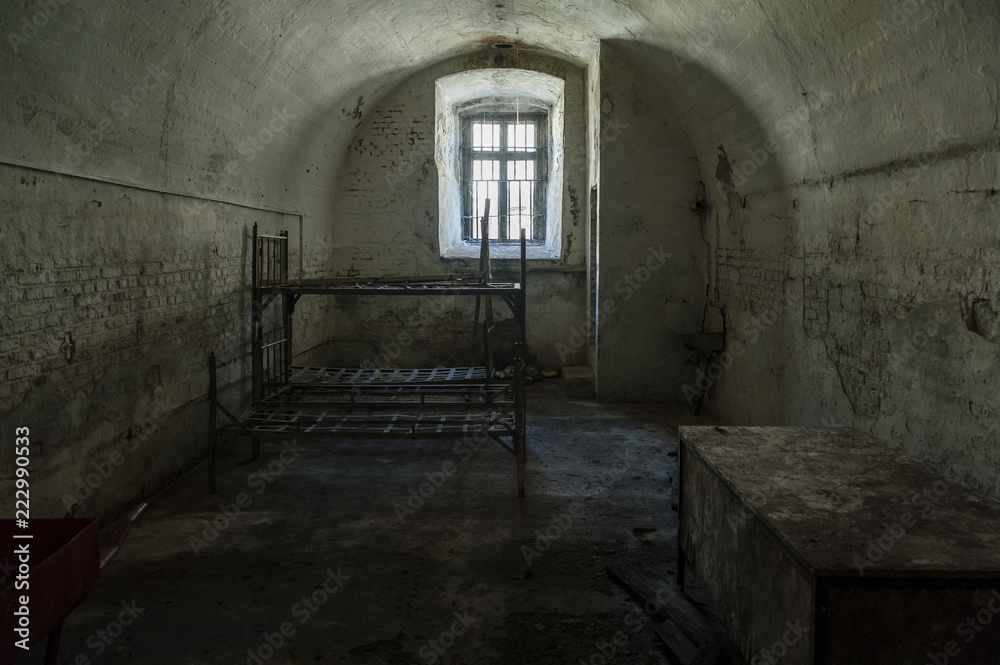Old prison cell/abandoned prison cell with metal bunk beds and sitting platform and steel bars at the small window.