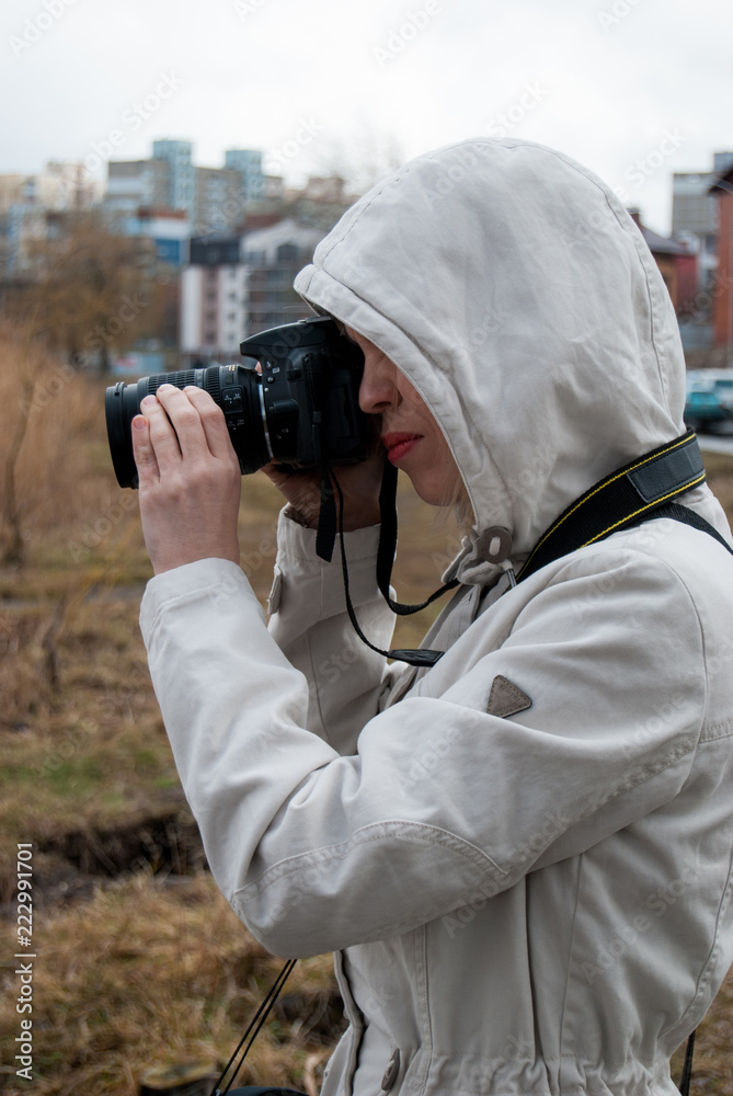 A girl in a white jacket takes pictures of nature near the lake A girl in a white jacket takes pictures of nature near the lake