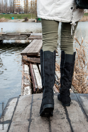 .Women's legs in tall black boots that go along rotten wooden boards