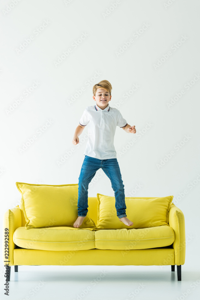 adorable boy having fun and jumping on yellow sofa on white adorable boy having fun and jumping on yellow sofa on white