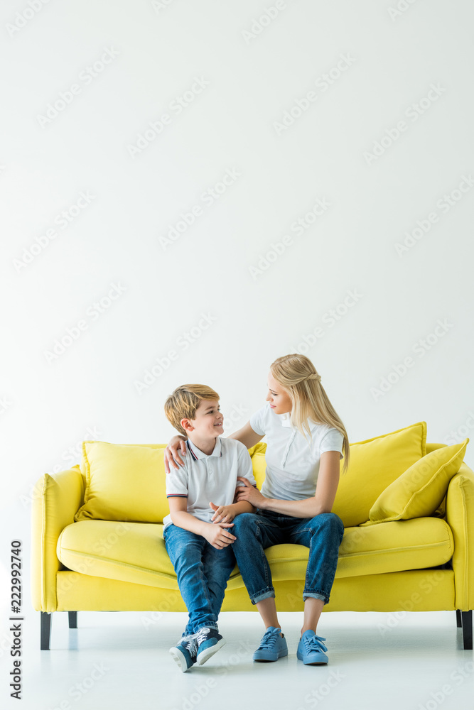 mother hugging happy son on yellow sofa on white