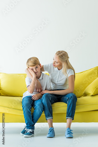 mother hugging upset son on yellow sofa on white