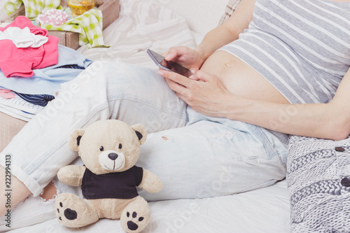 Pregnant woman with a teddy bear and various clothes for a newborn
