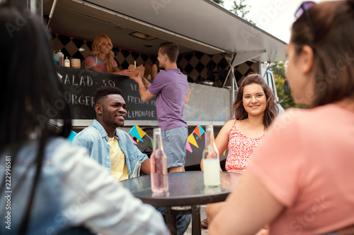 leisure and people concept - happy friends with drinks sitting at table at food truck