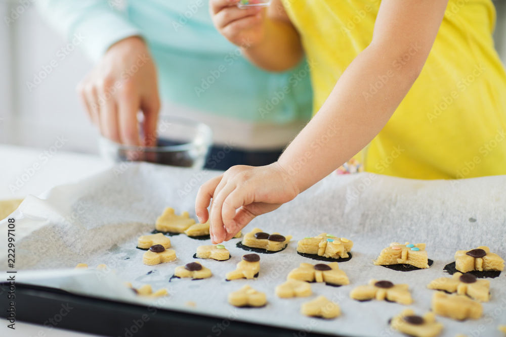 family, cooking and baking concept - mother and little daughter with sprinkles decorating cookies on tray at home kitchen family, cooking and baking concept - mother and little daughter with sprinkles decorating cookies on tray at home kitchen