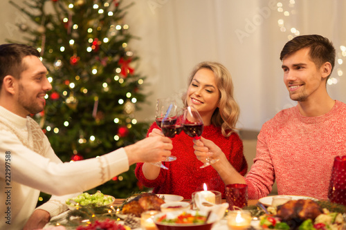 holidays and celebration concept - happy friends having christmas dinner at home  drinking red wine and clinking glasses