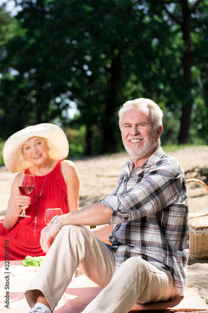 Romantic picnic. Cheerful confident aged man smiling while having a picnic with his happy wife