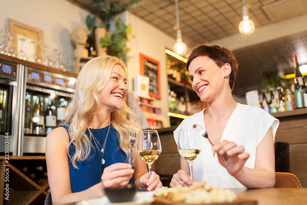 leisure, people and lifestyle concept - happy women eating snacks at wine bar or restaurant