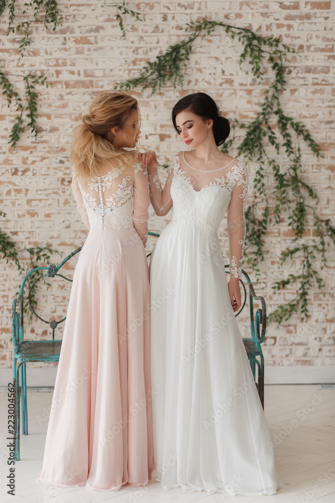 Full length portrait of two attractive young women in wedding dresses on rustic brick wall background. Gay lesbian concept
