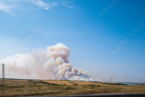 a big cloud of thick smoke rising from the ground to the clear blue sky on a summer day
