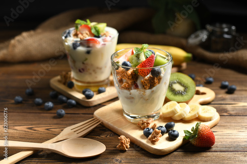 Yogurt with granola and fruits in glass on wooden table