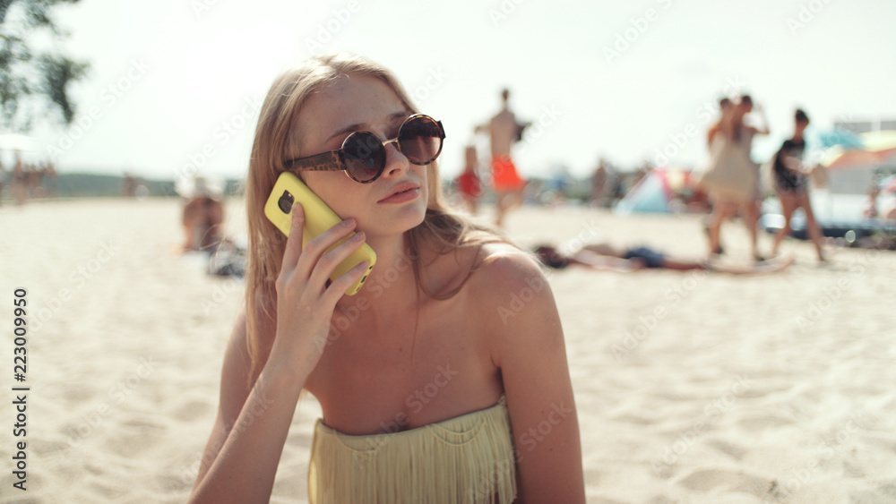 Pretty woman in bikini talking on phone at beach.