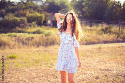 Fototapeta Naklejka Na Ścianę i Meble -  beautiful young woman in dress and sunglasses having fun with hair outdoor in countryside on a warm summer day