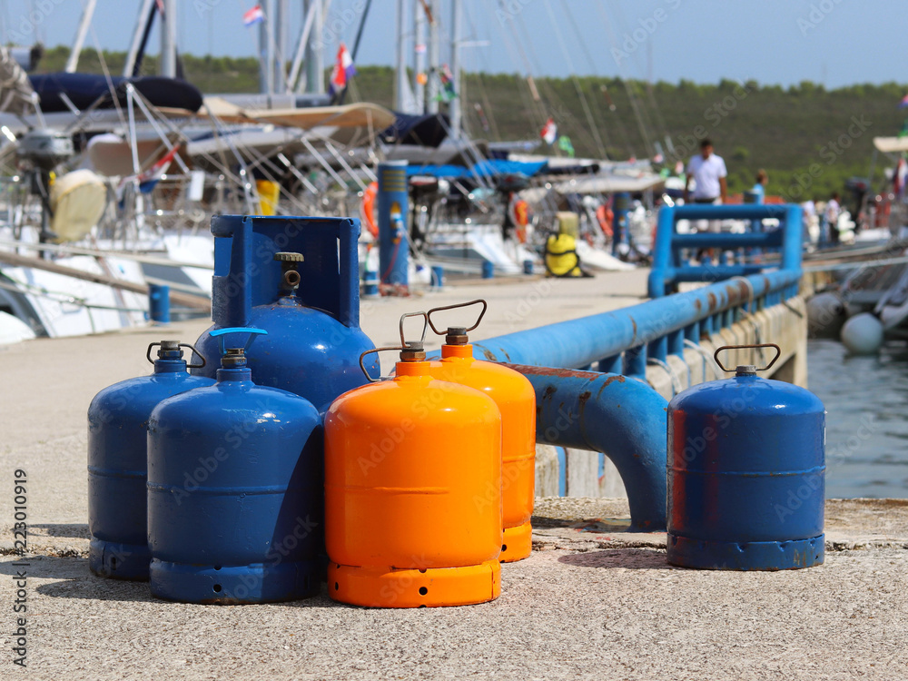 Tourist gas cylinders Stand on the pier in the marina against the backdrop of sailing yachts. Preparations for a charter cruise. Camp tanks under pressure. Energy is pumped from petroleum products.