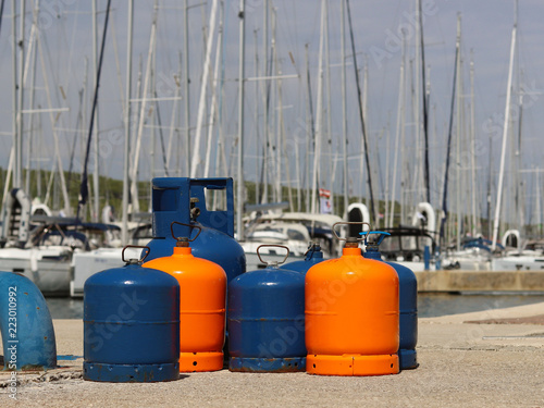 Tourist gas cylinders Stand on the pier in the marina against the backdrop of sailing yachts. Preparations for a charter cruise. Camp tanks under pressure. Energy is pumped from petroleum products.