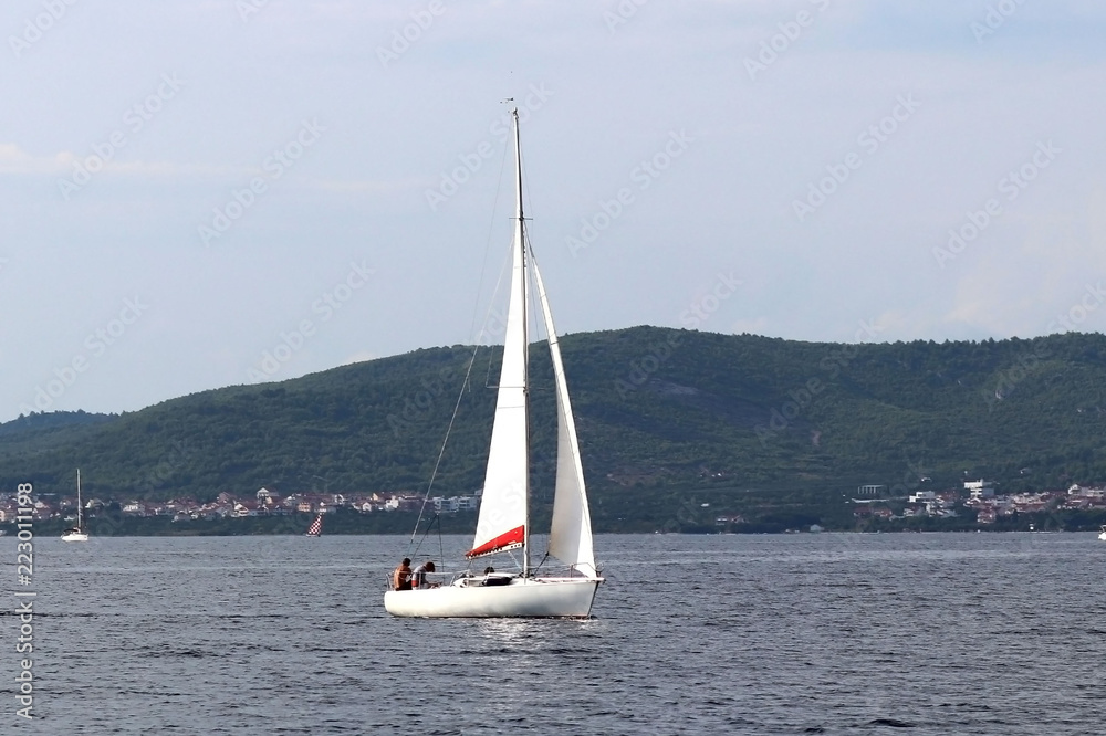 A small sailing sports yacht of daytime sailing is sailing with three yachtsmen along the coast of Croatia. Water sports and summer vacation on the water on a sunny summer day. A fascinating lifestyle