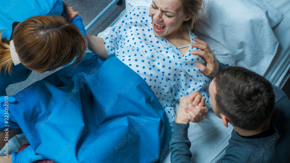 Photography In the Hospital Woman in Labor Pushes to Give Birth, Obstetricians Assisting, Husband Holds Her Hand for Support