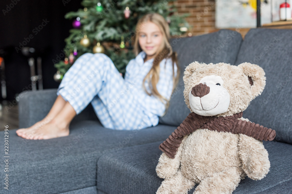 close-up view of teddy bear and child in pajamas sitting on couch behind at christmas time close-up view of teddy bear and child in pajamas sitting on couch behind at christmas time