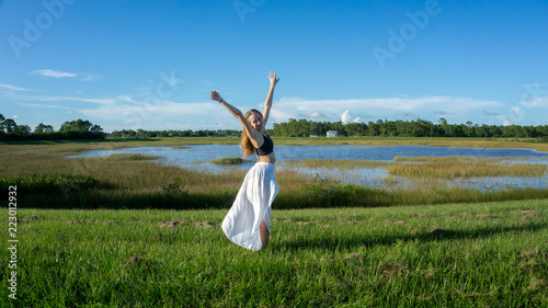 Blonde young woman standing backwards smiling in a beautiful field landscape outdoors with raise hands arms to the sky