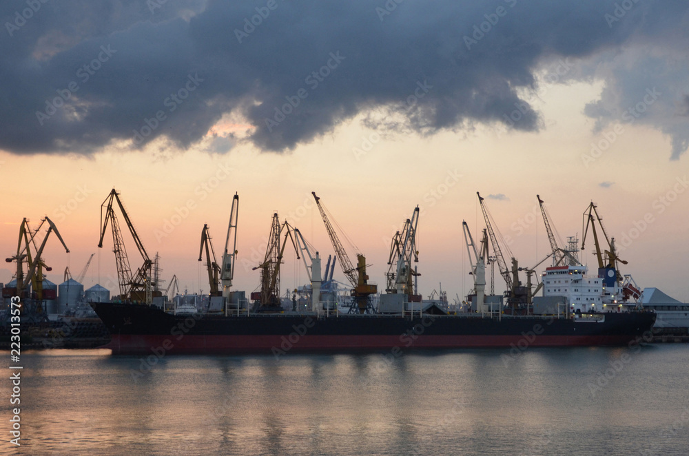 Cargo ship and cranes in the port, reflected in the water, twilight.