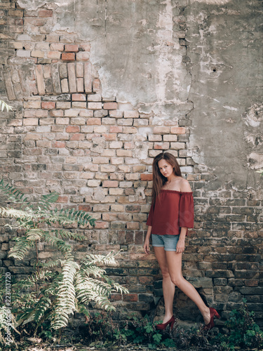 Long hair brunette woman standing at brick wall.