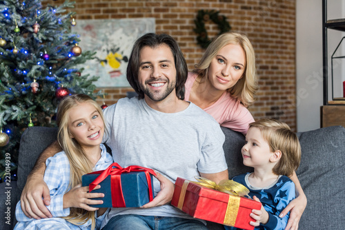 happy parents and cute children in pajamas holding christmas presents and smiling at camera