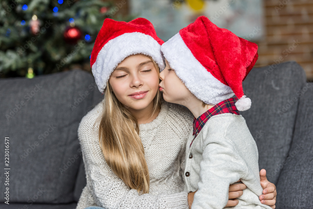 cute little boy in santa hat kissing sister at christmas time cute little boy in santa hat kissing sister at christmas time