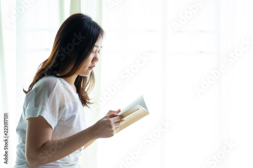 Asian women reading a book in a bedroom close up.