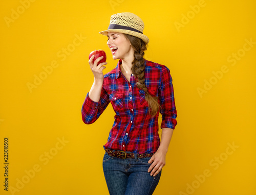 smiling young woman grower on yellow background eating an apple