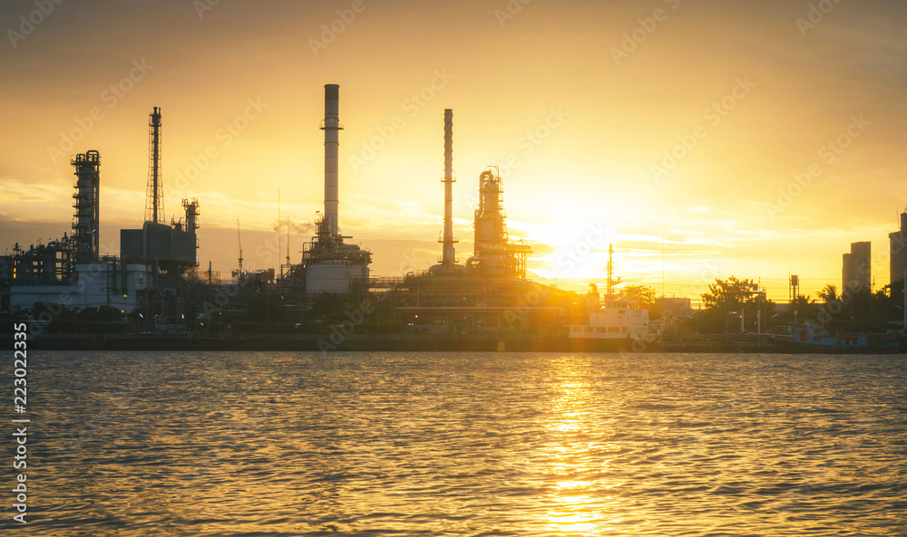 panorama view of petrochemical refinery oil energy plant factory industrial the fuel power storage design on morning skyline with sunshine at golden hour in sky with reflection on water riverside.