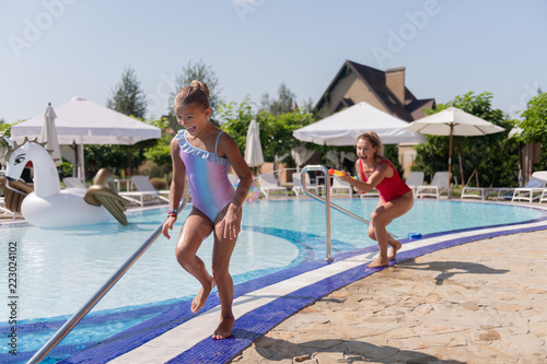 So much fun. Delighted happy girl running near the pool while playing with her mother