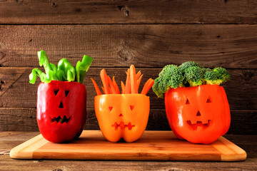 Healthy Halloween food. Vegetables for dipping in Jack o Lantern bell peppers. Side view against rustic wood.
