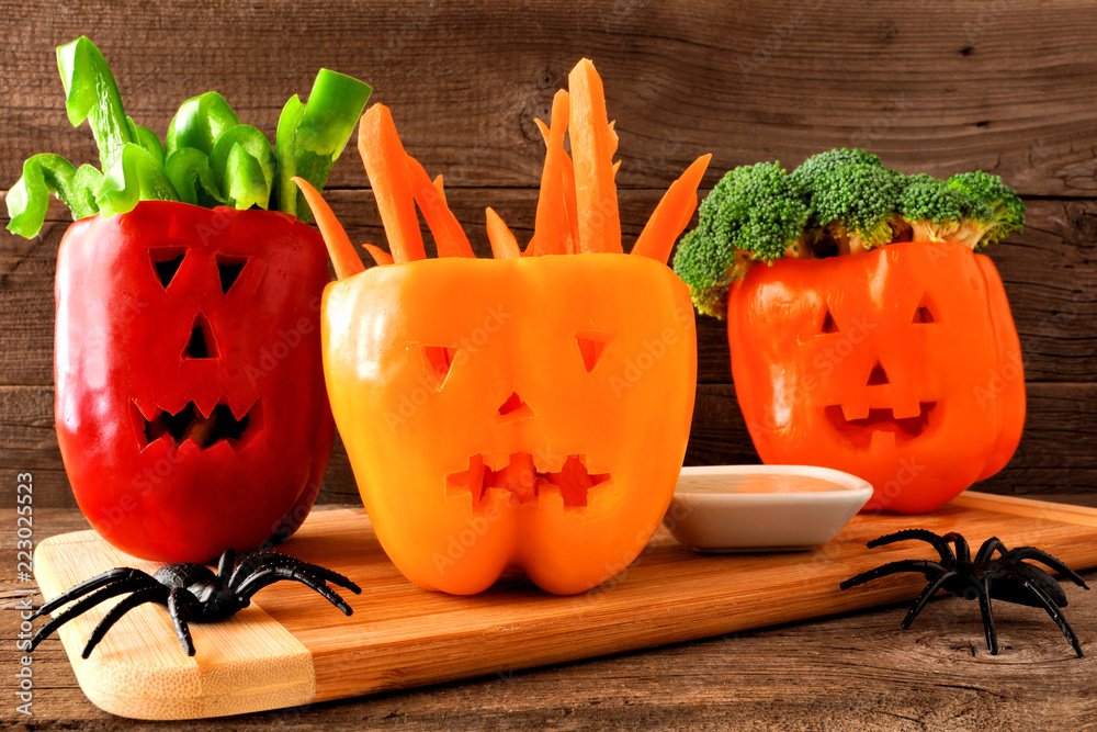 Obraz premium Healthy Halloween food. Vegetables and dip in Jack o Lantern bell peppers. Close up against rustic wood.
