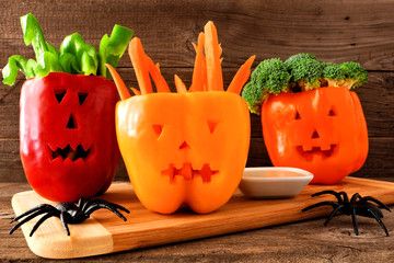 Healthy Halloween food. Vegetables and dip in Jack o Lantern bell peppers. Close up against rustic wood.