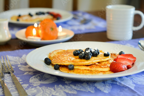 Pancakes on a breakfast table with blueberries and strawberries.