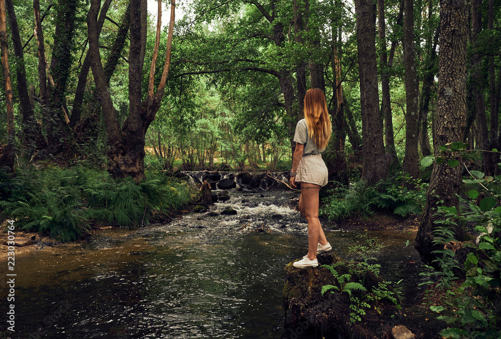 Young woman standing on shore of forest river Young woman standing on shore of forest river
