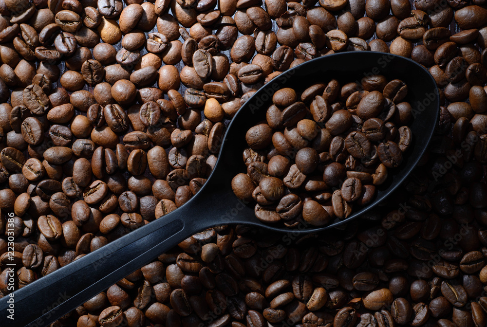 Fototapeta premium Coffee. Black spoon with coffee on old brown table studded with coffee